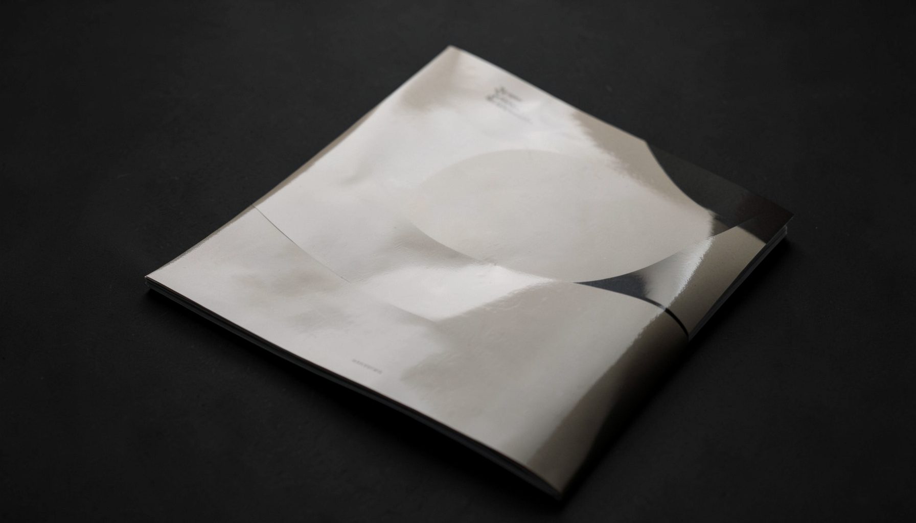 A glossy magazine cover lying on a dark surface, lit by soft studio light with elegant neutral tones