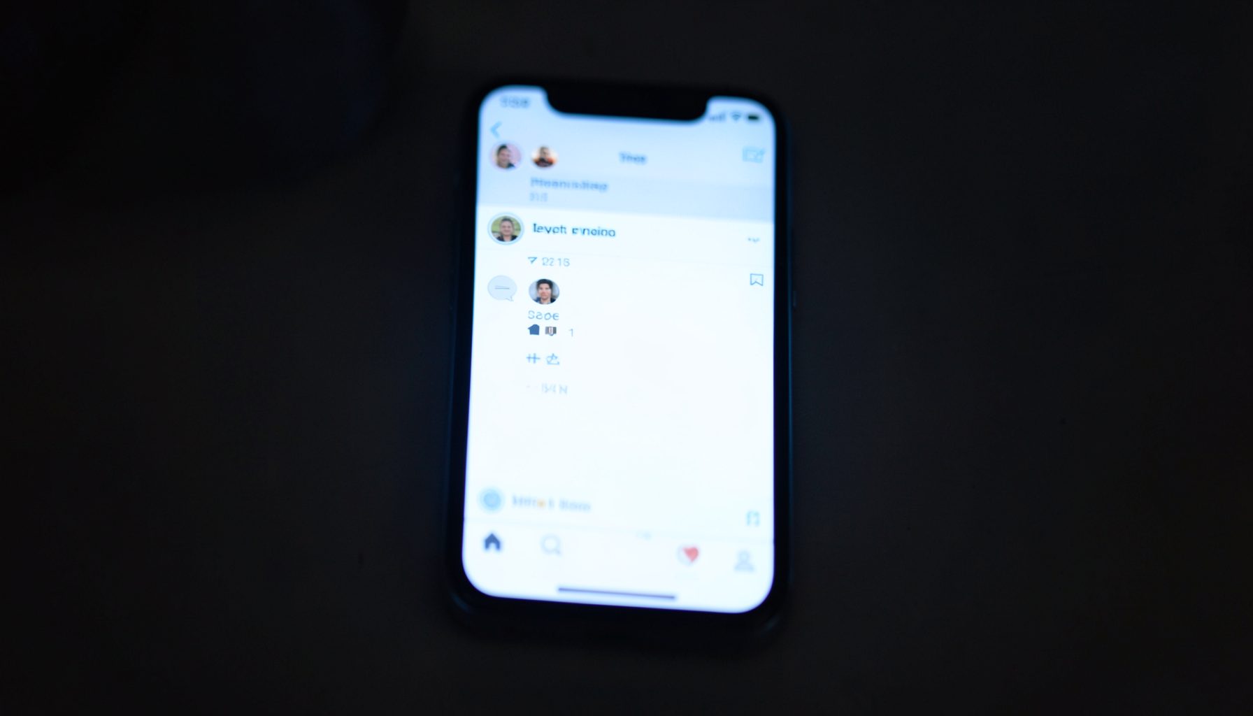 A smartphone screen glowing in a dim room displaying a social media interface in soft white and blue tones