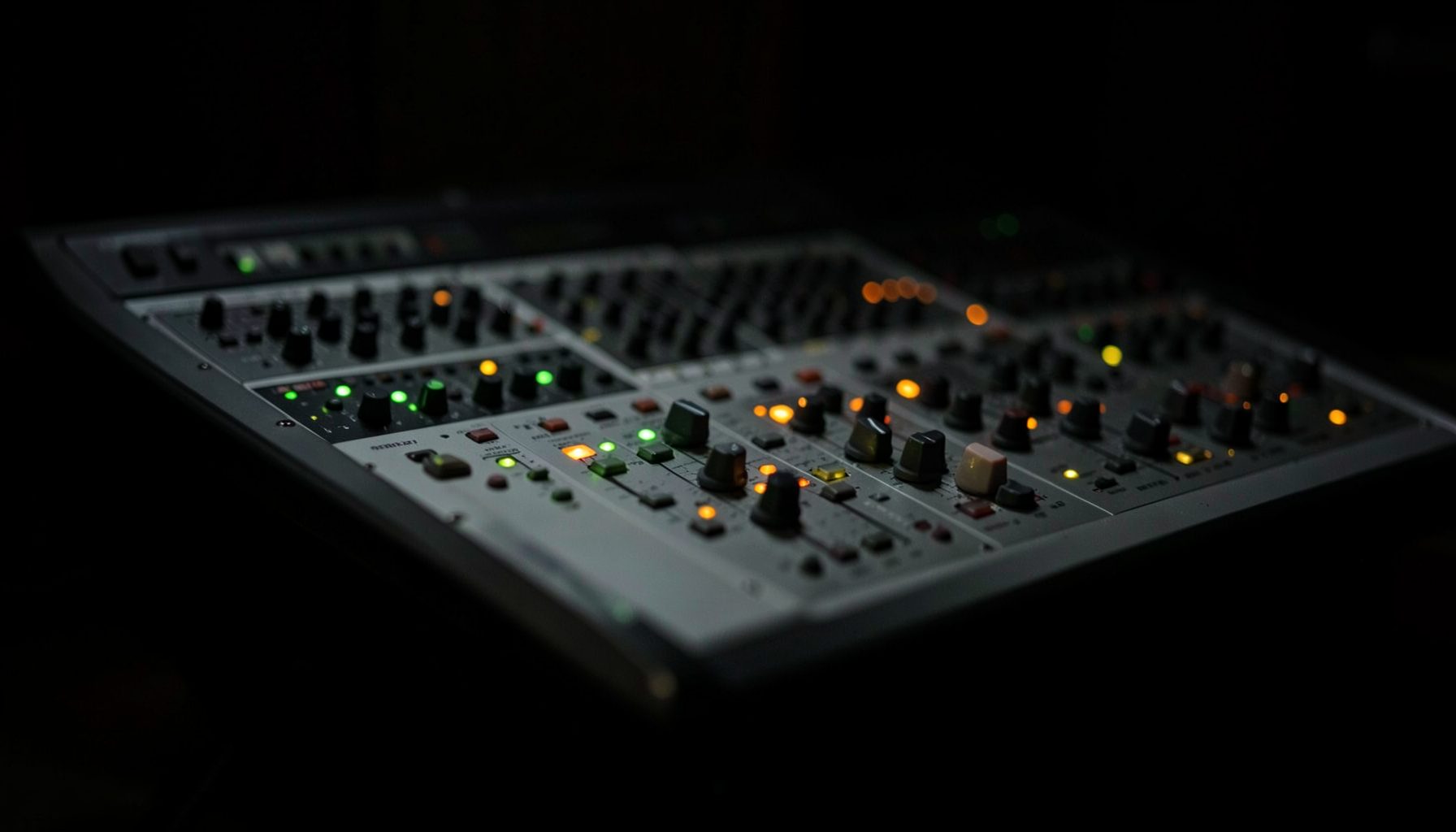 A studio mixing console with subtle green and amber indicator lights in a darkened room