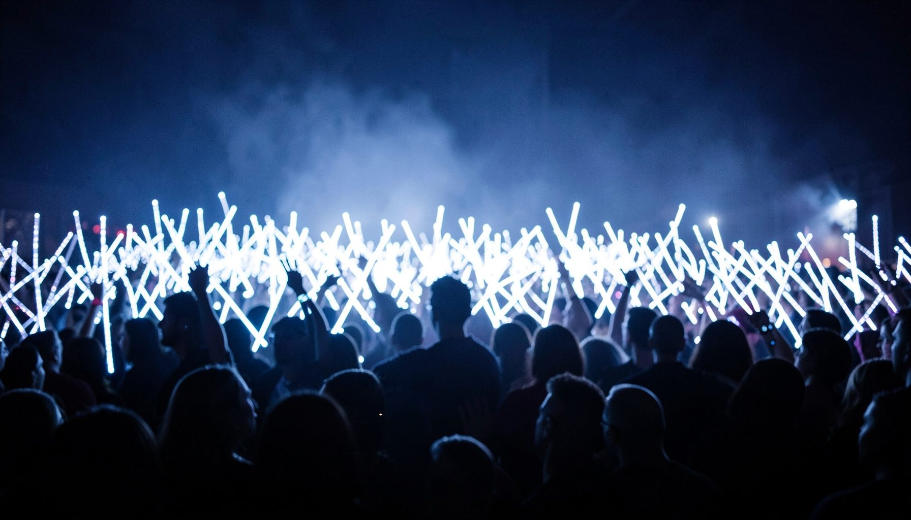 Concert crowd silhouettes against a sea of glowing white light sticks, creating a dreamy fan atmosphere