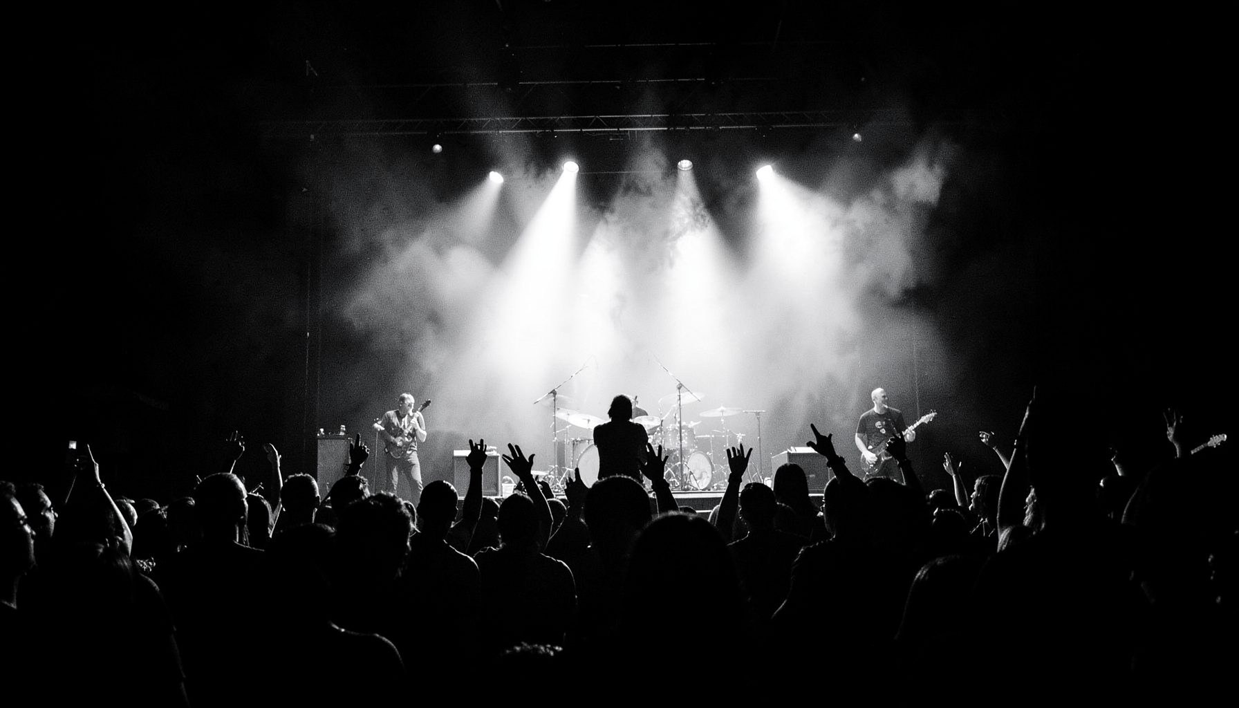 Dramatic black-and-white concert stage with silhouetted performers against bright spotlights, moody and high-contrast